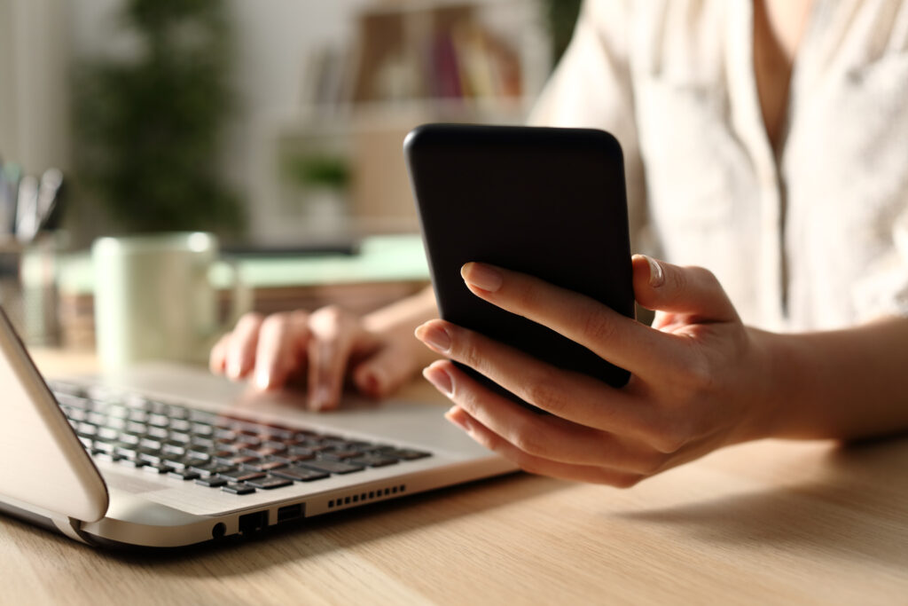 Vrouw die telefoon vasthoudt en achter haar laptop aan het werk is